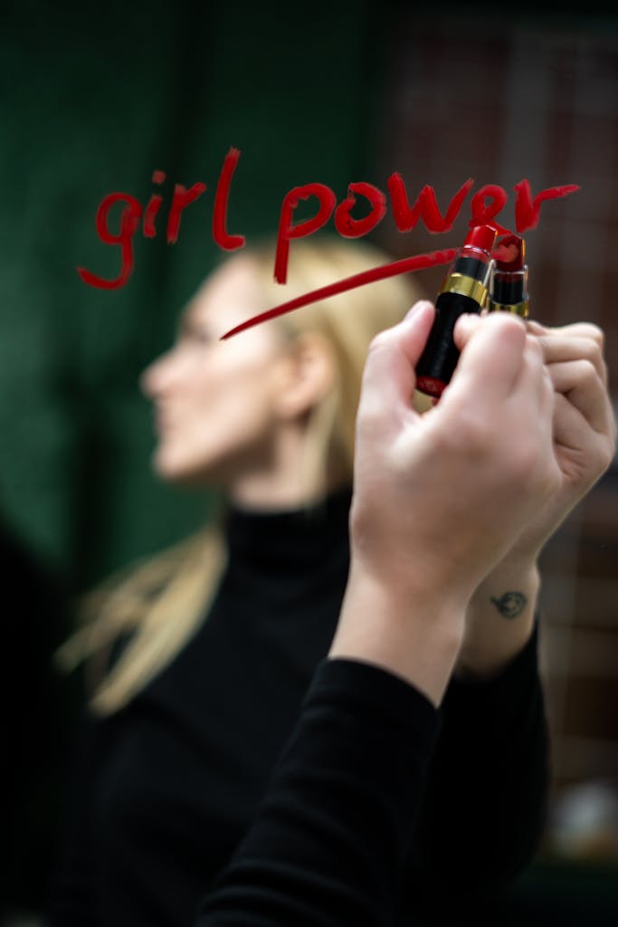 Close-up of a woman writing 'girl power' on a mirror with lipstick.