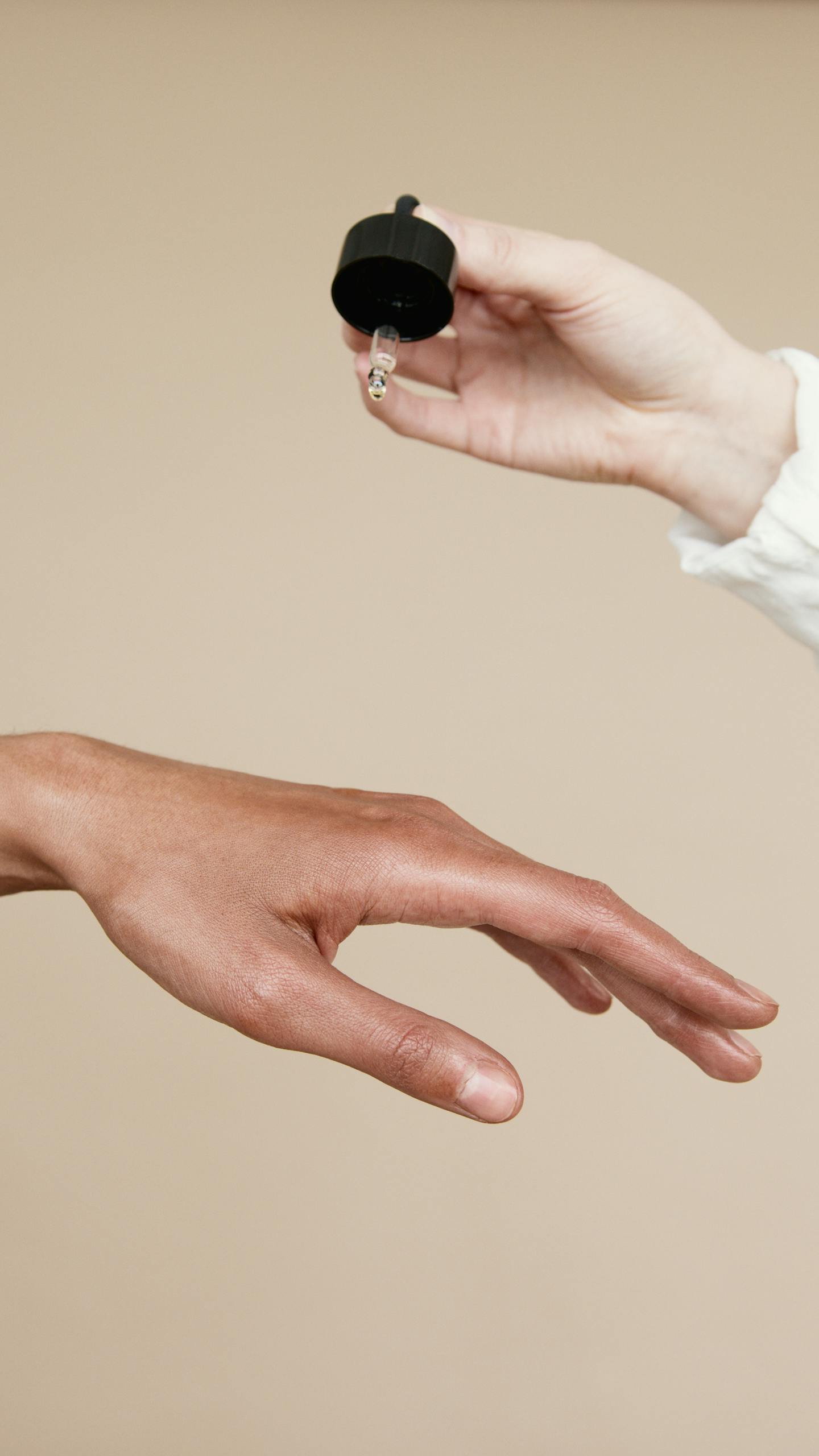 Two hands applying skin care oil with a dropper. Ideal for wellness and beauty themes.
